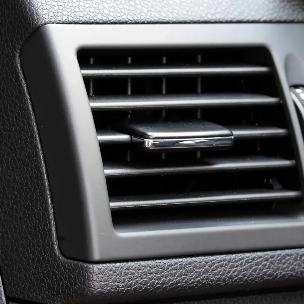 Grille d'aération voiture : ventilation habitacle auto Grille d'aération de voiture noire avec curseur de réglage chromé sur un tableau de bord texturé.