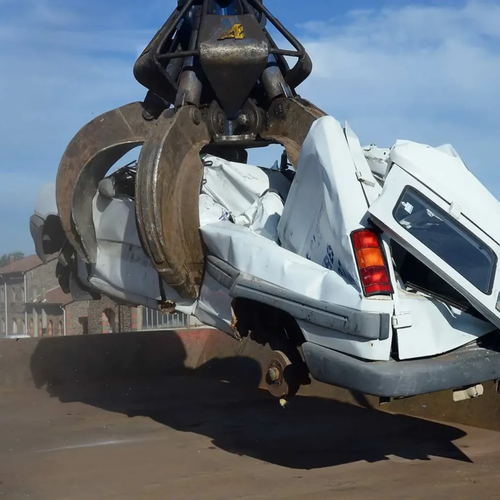 Recyclage auto : une pince broie une vieille camionnette Pince de ferrailleur soulevant une fourgonnette blanche accidentée dans une casse automobile pour recyclage.