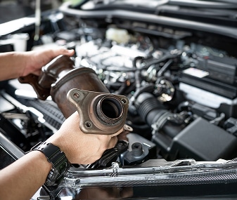 Remplacement d'un pot catalytique sur un moteur de voiture Mécanicien tenant un pot catalytique au-dessus du moteur ouvert d'une voiture lors d'une réparation automobile.